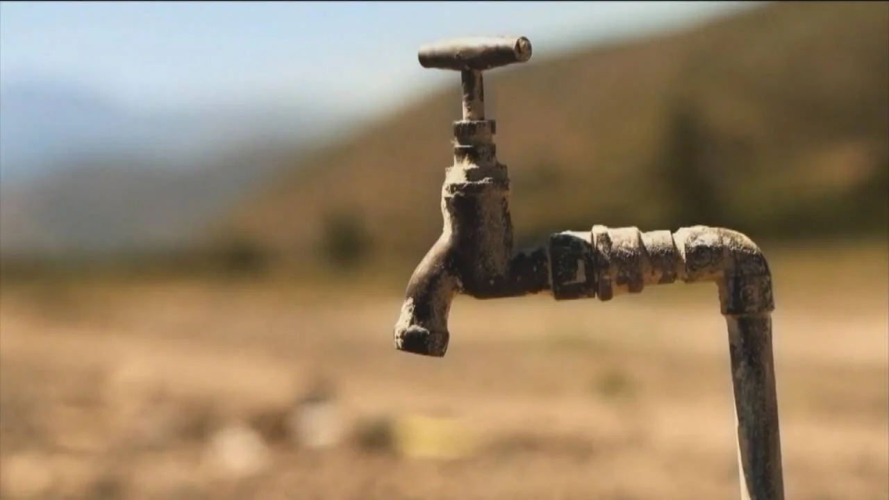 Canilla de metal oxidada y seca en un paisaje árido, simbolizando la escasez de agua potable.