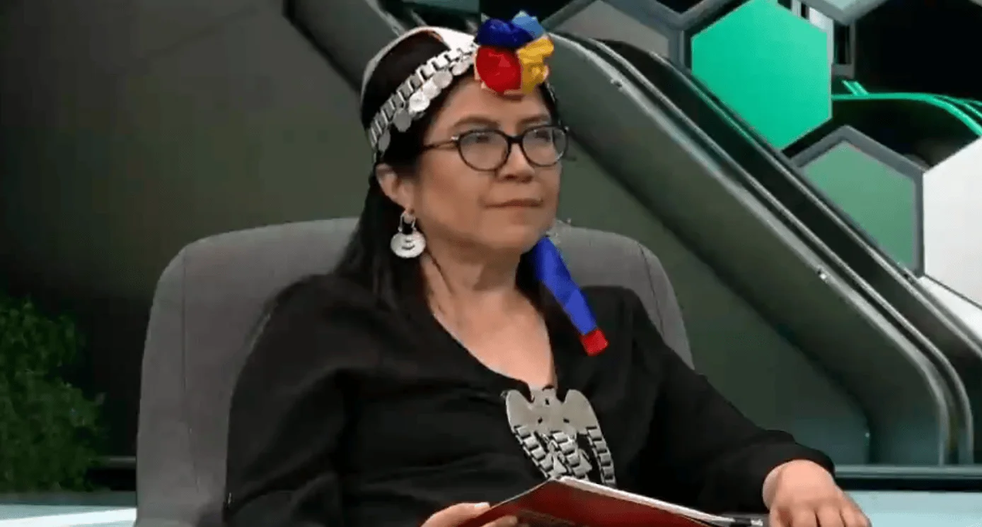 Mujer con indumentaria tradicional mapuche, incluida vincha de plata y joyería, sentada en un estudio de televisión.