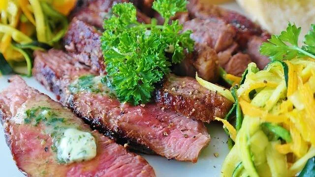 Rebanadas de carne a la parrilla en su punto, con mantequilla de hierbas y guarnición de verduras salteadas.