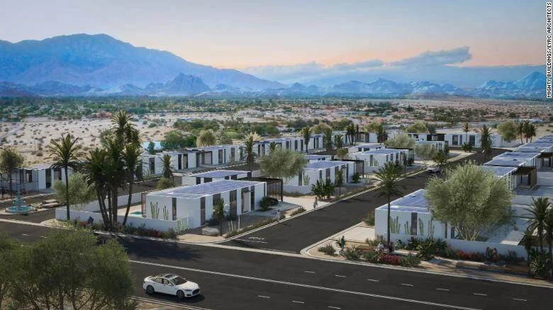 Vista aérea de un proyecto residencial con casas modulares blancas y paneles solares rodeadas de vegetación desértica y montañas al fondo.
