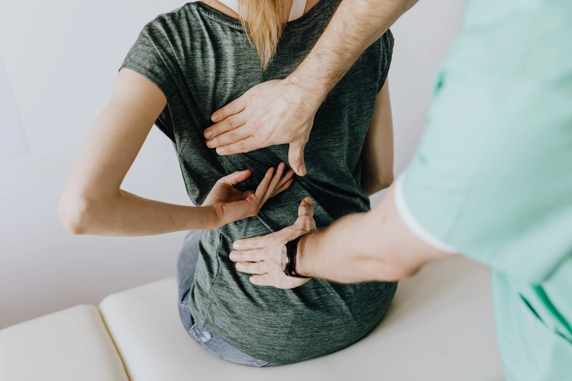 Un profesional de la salud palpa la espalda de una mujer sentada durante una consulta médica o fisioterapéutica.