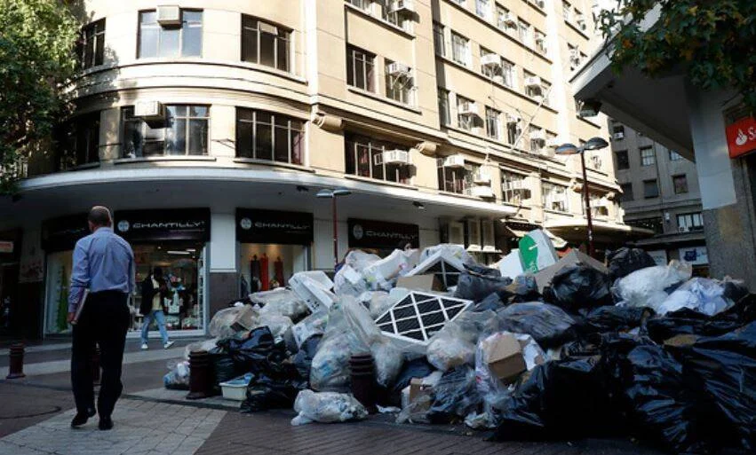 Gran montaña de bolsas de basura y residuos acumulados en la vereda de una calle comercial del centro de la ciudad.