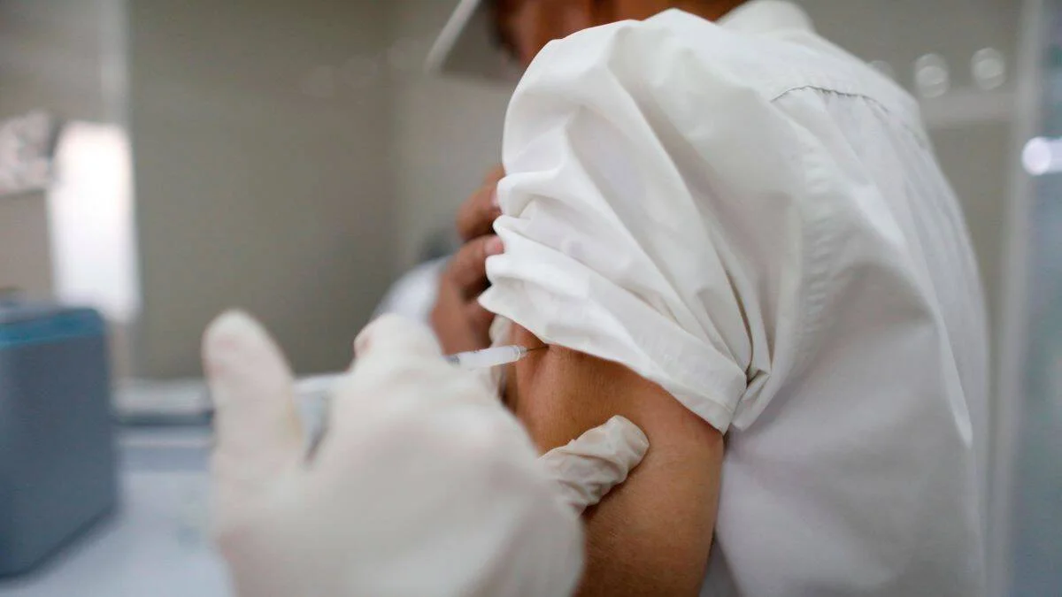 Personal de salud con guantes administra una inyección en el brazo de una persona con camisa blanca arremangada.