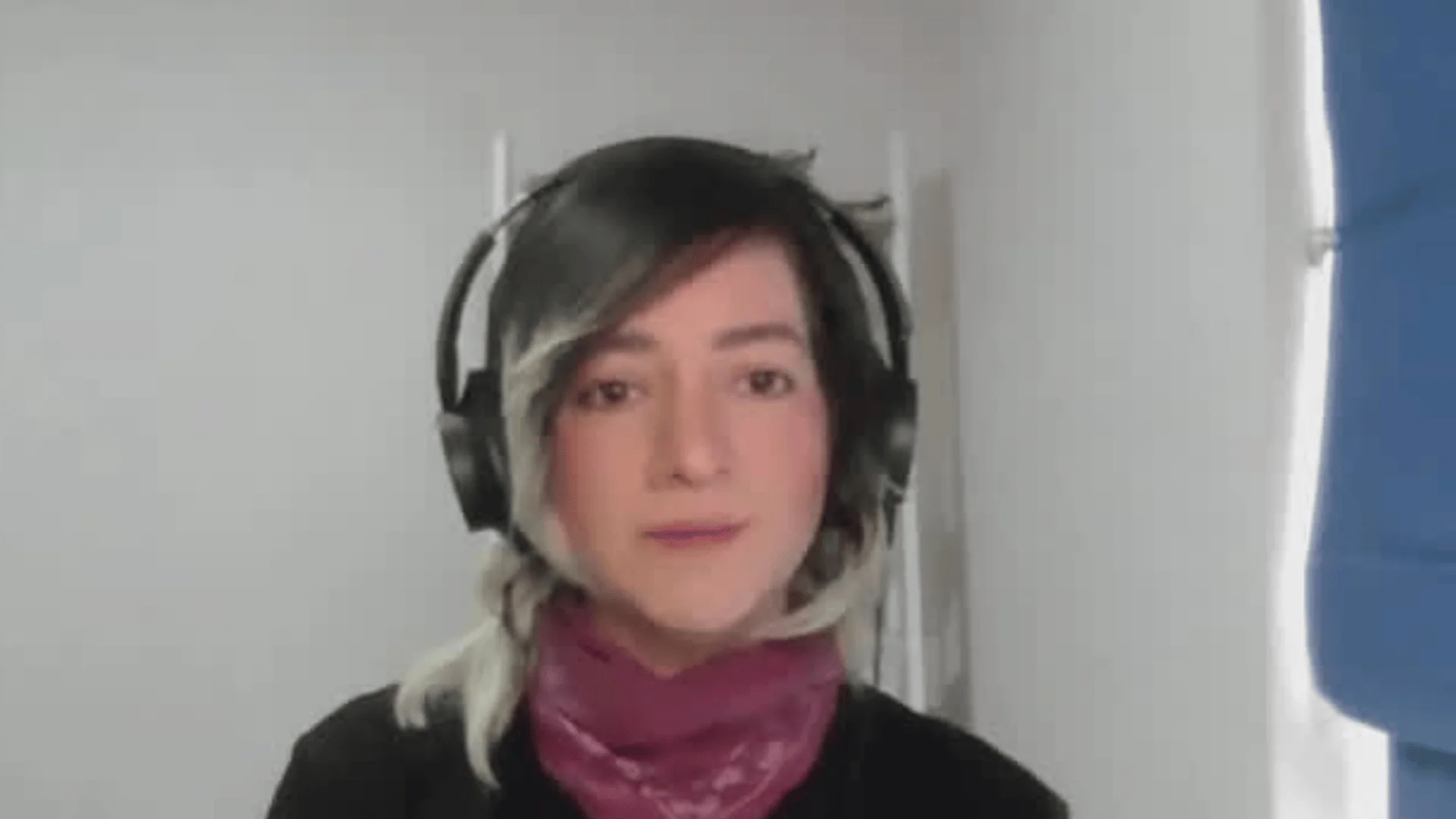 Mujer con auriculares negros y pañuelo rosa participa en una videollamada desde un espacio interior.
