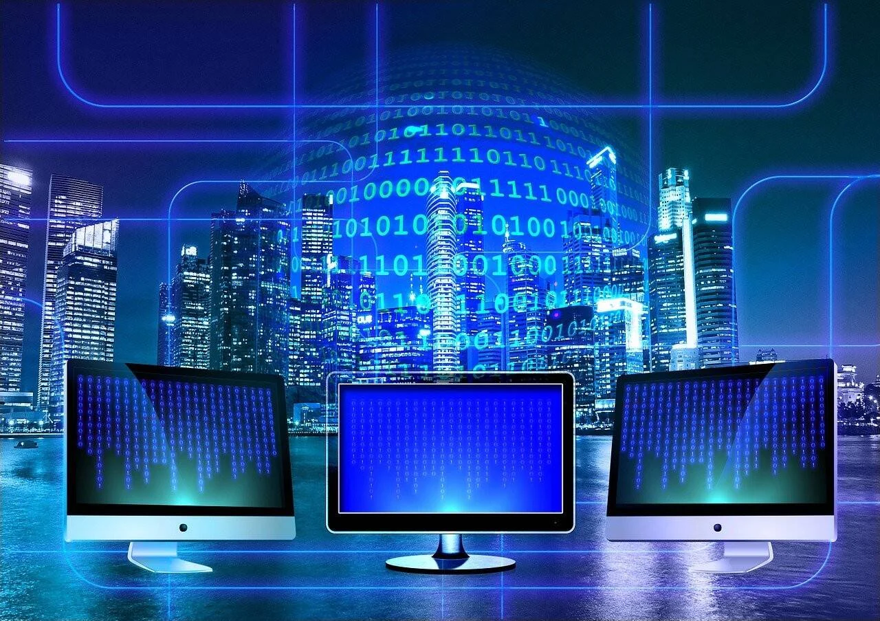 Tres monitores de computadora frente a un skyline nocturno con código binario superpuesto, representando conectividad digital urbana.