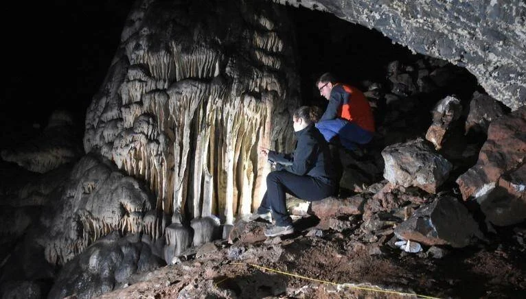 Dos investigadores observan de cerca formaciones de estalactitas y estalagmitas en el interior de una cueva oscura.