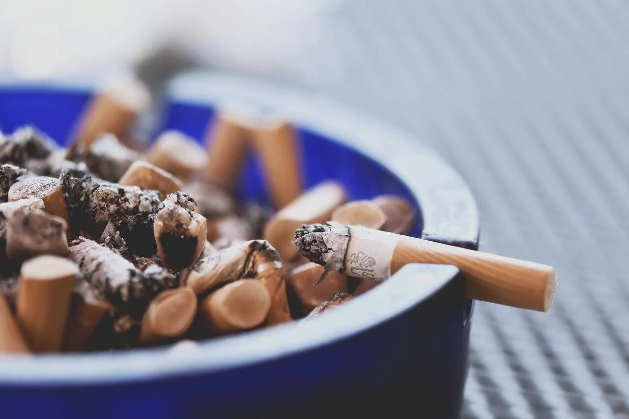 Cenicero azul repleto de colillas de cigarrillos apagadas, con una colilla apoyada en el borde.