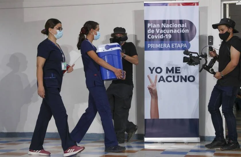 Dos enfermeras con mascarilla transportan una caja térmica azul junto a un cartel del Plan Nacional de Vacunación Covid-19 que dice 'Yo me vacuno'.