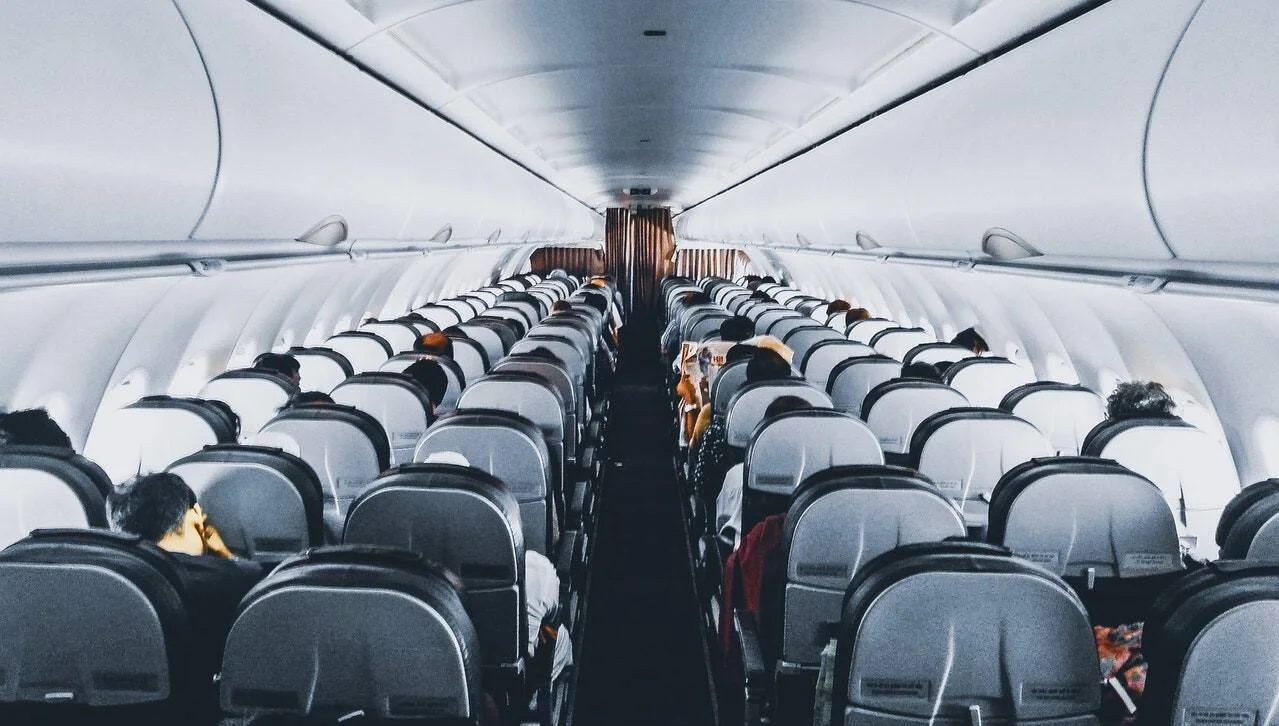 Vista del pasillo central de un avión comercial con todos los asientos ocupados por pasajeros en clase económica.
