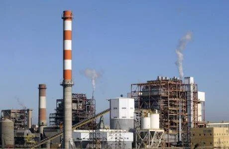 Complejo industrial con chimeneas de franjas rojas y blancas emitiendo humo bajo un cielo azul despejado.