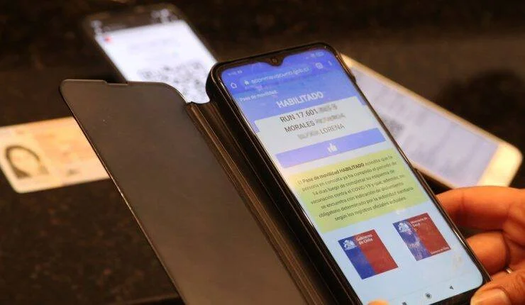 Mano sosteniendo un teléfono que muestra el pase de movilidad habilitado del Gobierno de Chile junto a una cédula de identidad.
