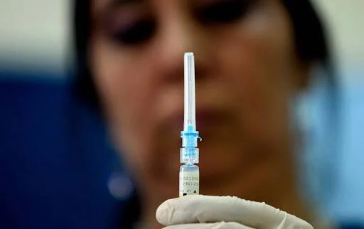 Trabajadora de salud con guante sostiene una jeringa lista para aplicar una vacuna.