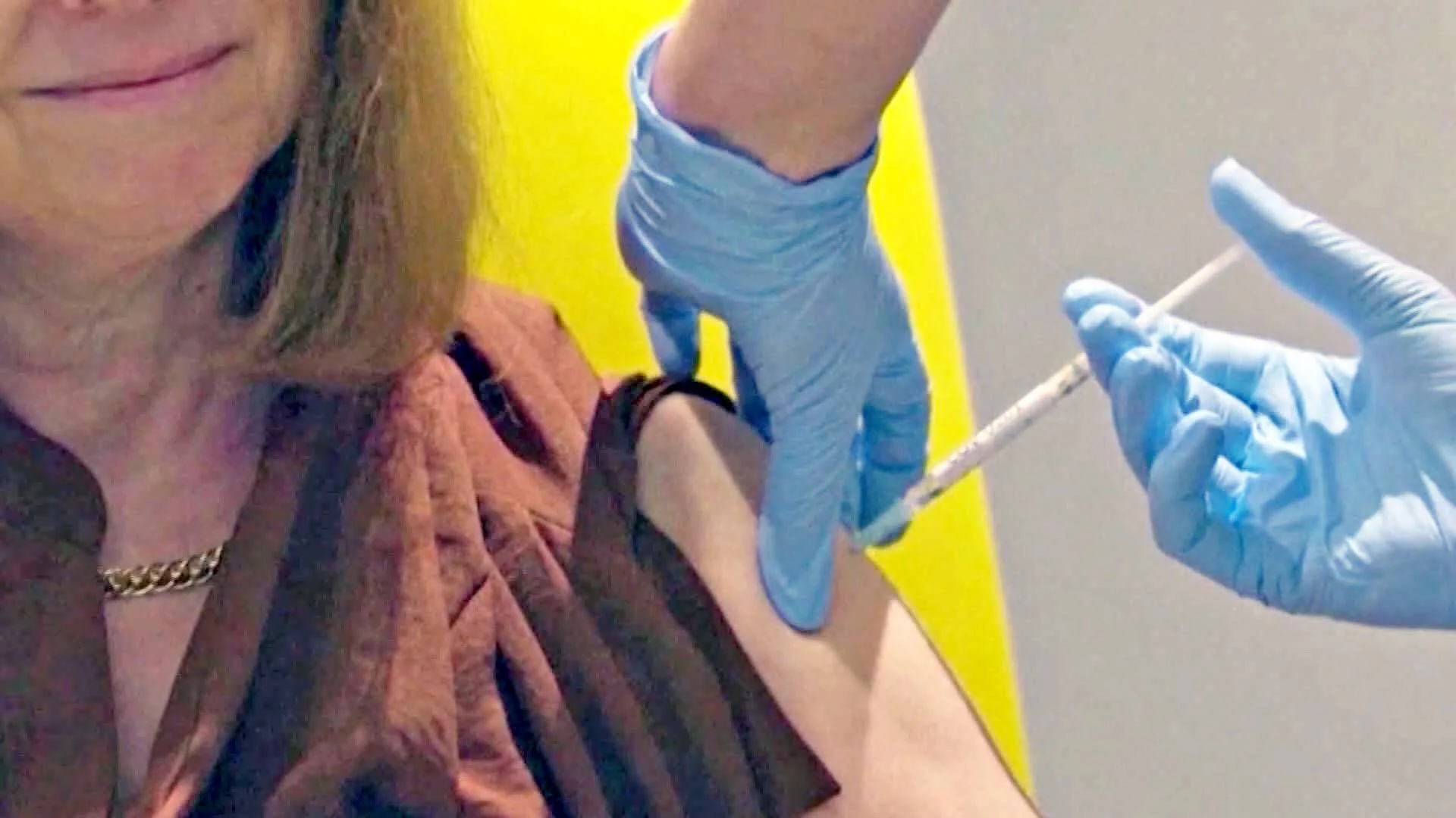 Personal sanitario con guantes azules administra una inyección en el brazo de una mujer mayor que sonríe.