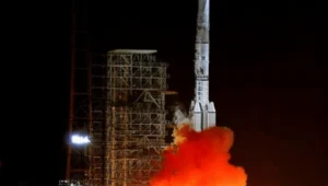 Cohete chino despega de noche desde su plataforma de lanzamiento entre grandes llamas y nubes de humo naranja.