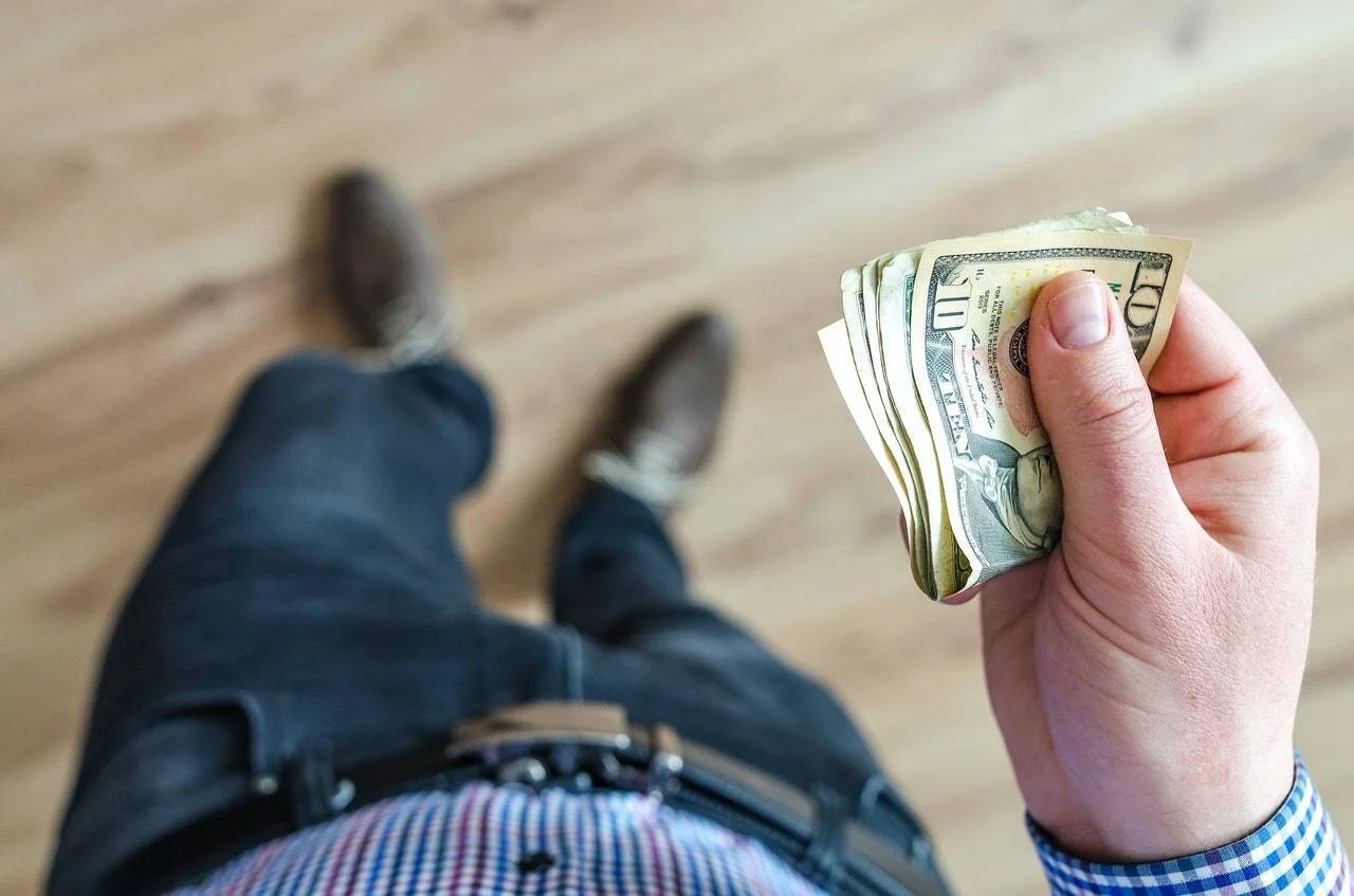 Una mano sostiene un fajo de billetes de dólar estadounidense visto desde la perspectiva de quien los lleva.