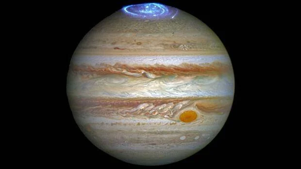 Imagen del planeta Júpiter captada por el telescopio Hubble, mostrando una aurora azul en el polo norte y la Gran Mancha Roja en su superficie.