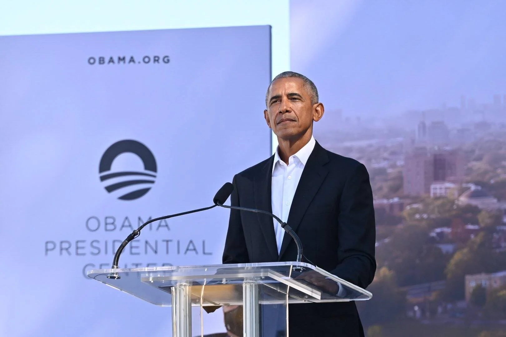 Un hombre habla en un podio frente a un cartel del Obama Presidential Center con el logo de obama.org.