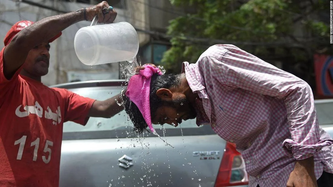 Un hombre vierte agua fría sobre la cabeza de otra persona en la calle para aliviar el calor extremo.