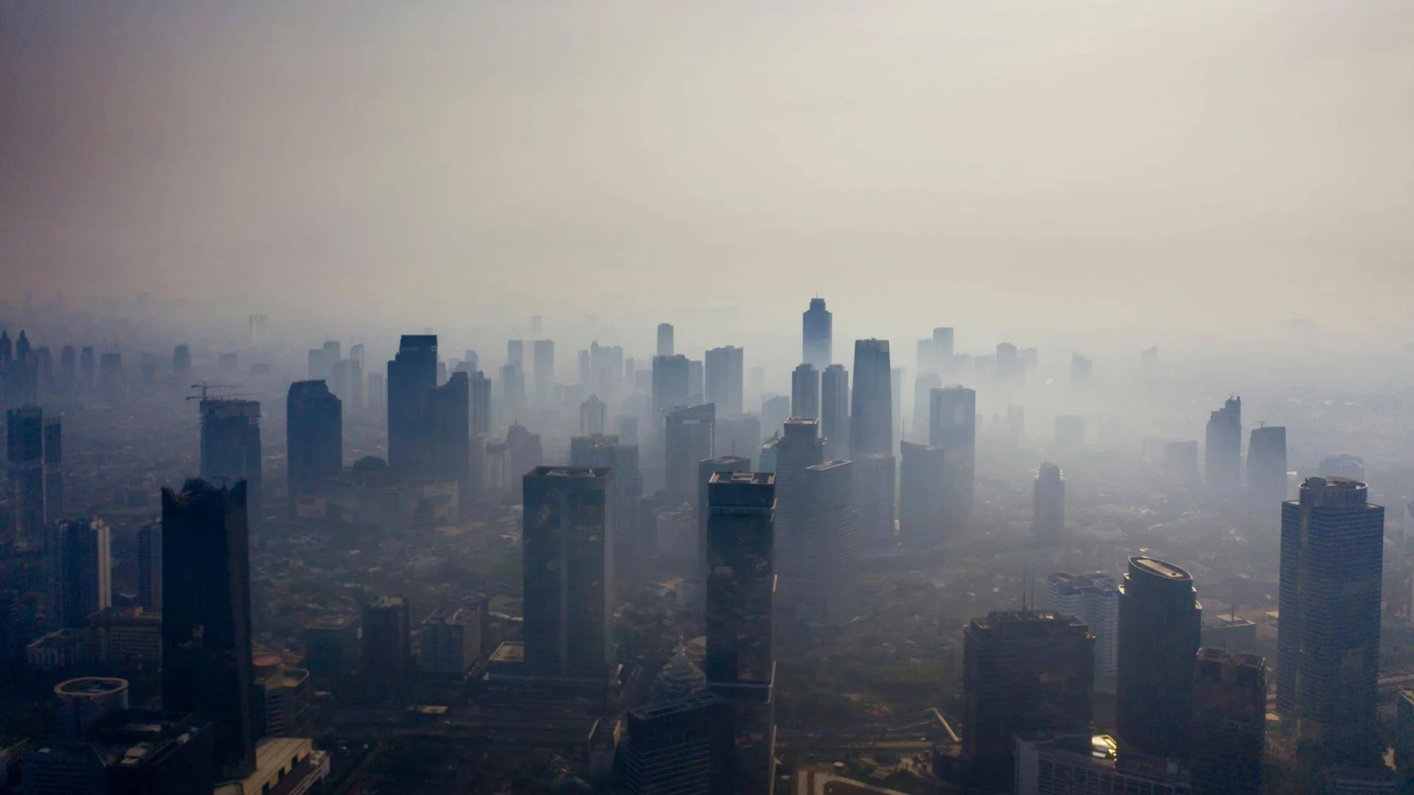Vista aérea de una gran ciudad con rascacielos envueltos en una densa capa de smog y contaminación atmosférica.