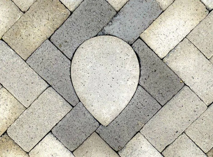 Pavimento de adoquines grises en espiga con una pieza central de forma ovalada o en lágrima.