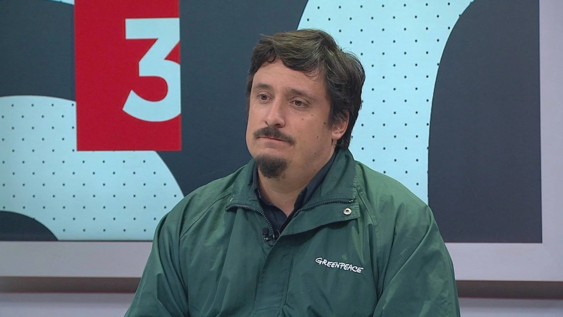 Hombre con chaqueta verde de Greenpeace concede una entrevista en un estudio de televisión.