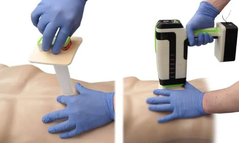 Dos manos con guantes quirúrgicos aplican un dispositivo médico portátil sobre el torso de un maniquí de entrenamiento.