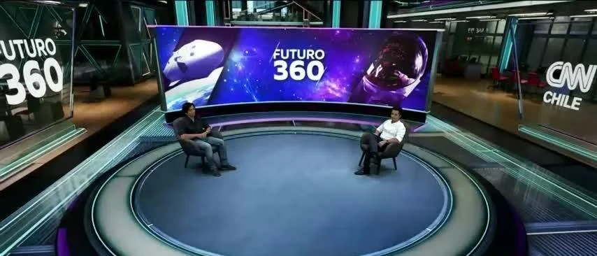 Dos conductores conversan sentados en el estudio del programa Futuro 360 de CNN Chile, con una pantalla curva de fondo temática espacial.