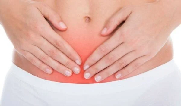 Persona sosteniendo su abdomen bajo con ambas manos, con área enrojecida que indica dolor o inflamación en la zona pélvica.