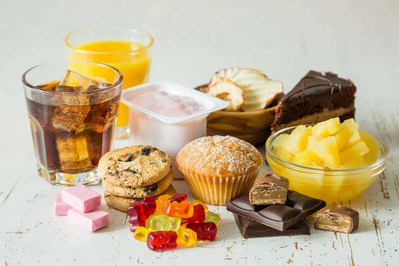 Selección de alimentos ultraprocesados con alto contenido de azúcar: gaseosa, jugo, muffin, galletas, chocolates, gomitas, yogur, tarta y piña en almíbar.
