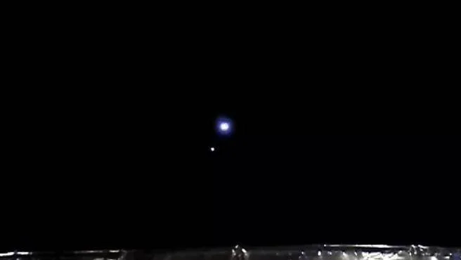 Dos puntos luminosos brillantes visibles en un cielo completamente oscuro sobre una superficie reflectante.
