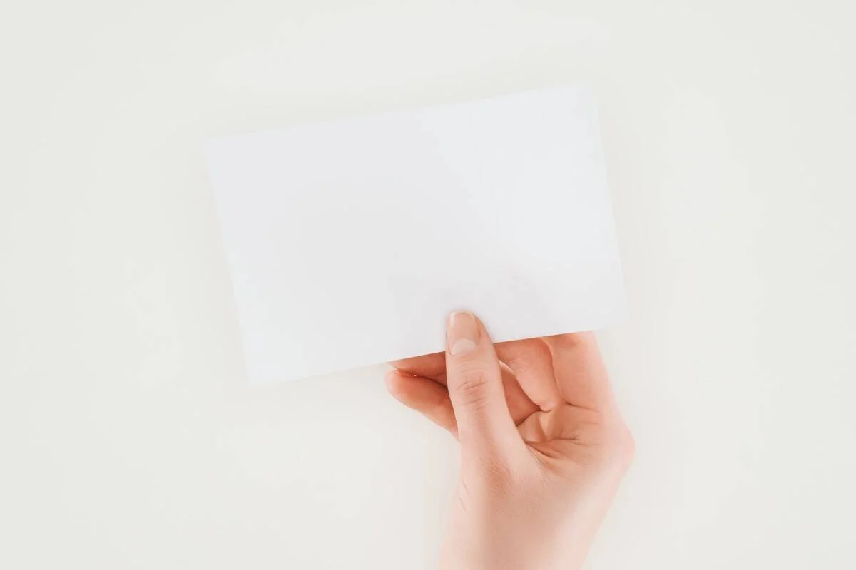 Una mano sujeta un sobre blanco cerrado sobre fondo claro.