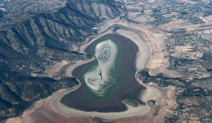Vista aérea de un embalse con nivel de agua muy bajo, rodeado de montañas áridas y tierras de cultivo.
