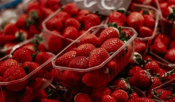 Fresas rojas maduras apiladas y en envases plásticos transparentes en un puesto de mercado.