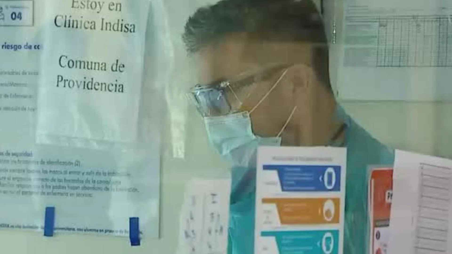 Trabajador de salud con mascarilla y gafas protectoras junto a carteles de la Clínica Indisa, Comuna de Providencia.