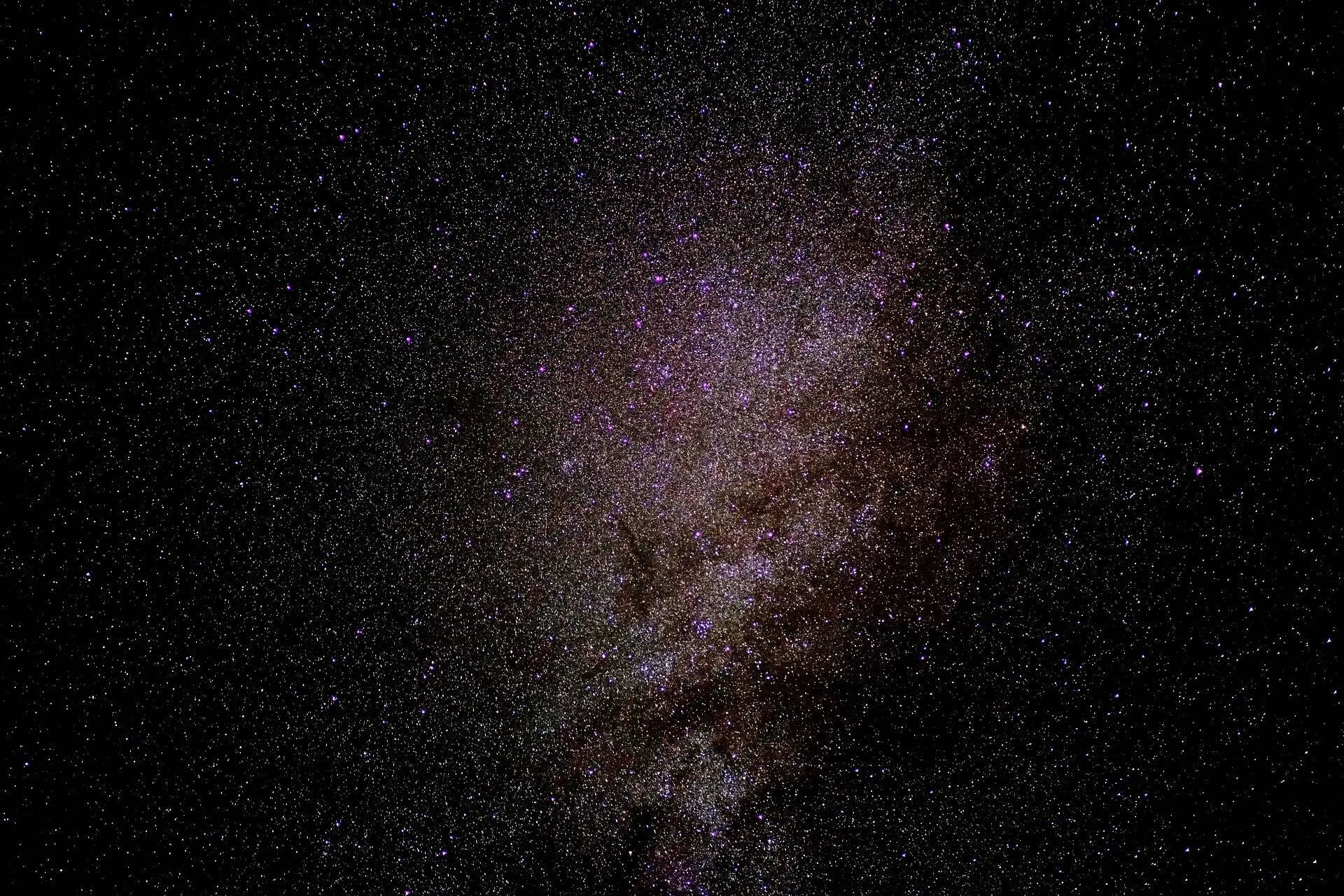 Densa concentración estelar de la Vía Láctea sobre cielo nocturno oscuro con tonos dorados y violetas.