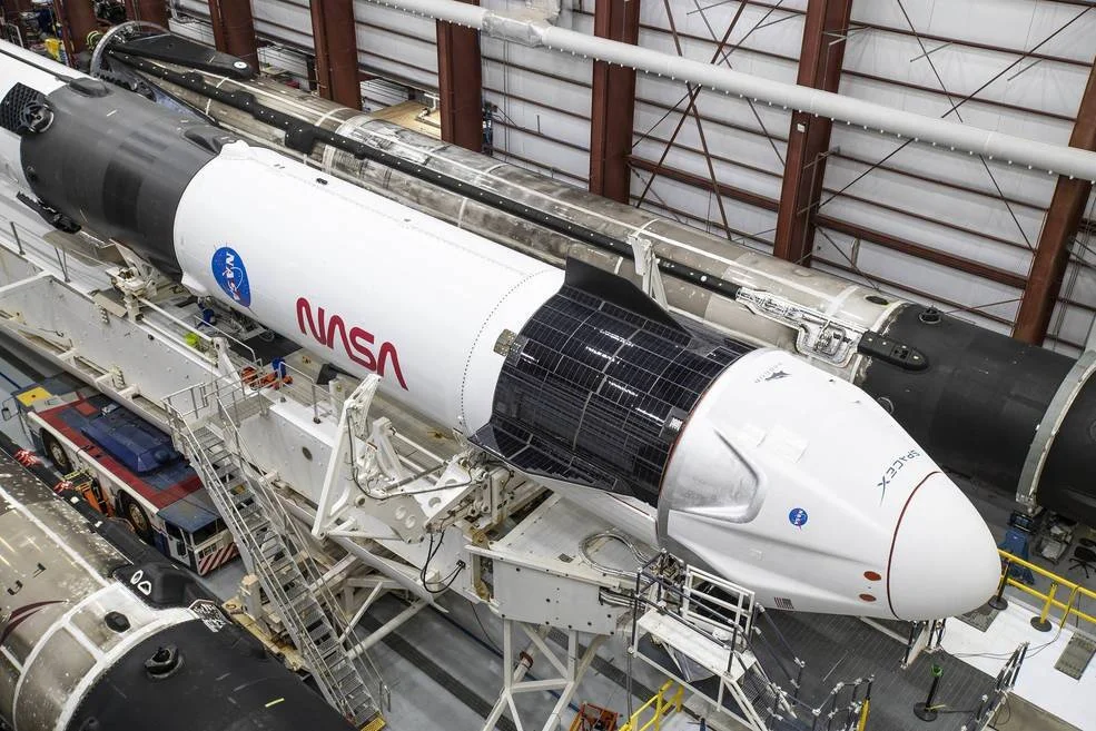 Cohete Falcon 9 de SpaceX con la cápsula Dragon y logo de la NASA, en posición horizontal dentro de un hangar antes del lanzamiento.