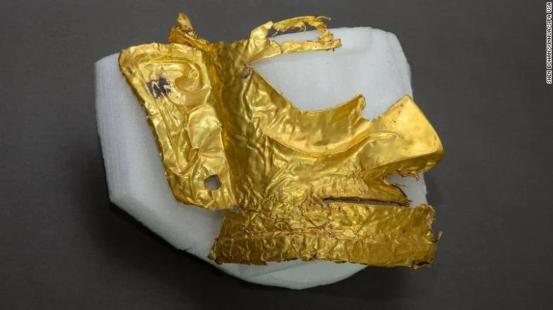 Fragmento de máscara de oro arrugada, posiblemente de origen arqueológico chino, apoyada sobre soporte de espuma blanca.
