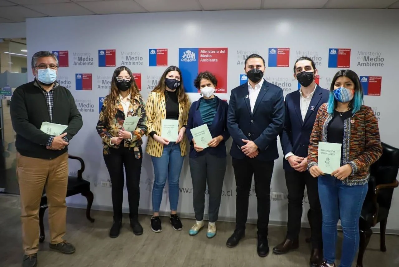 Siete personas con mascarilla posan sosteniendo documentos titulados 'Declaración Oficial 2022' frente al mural del Ministerio del Medio Ambiente de Chile.