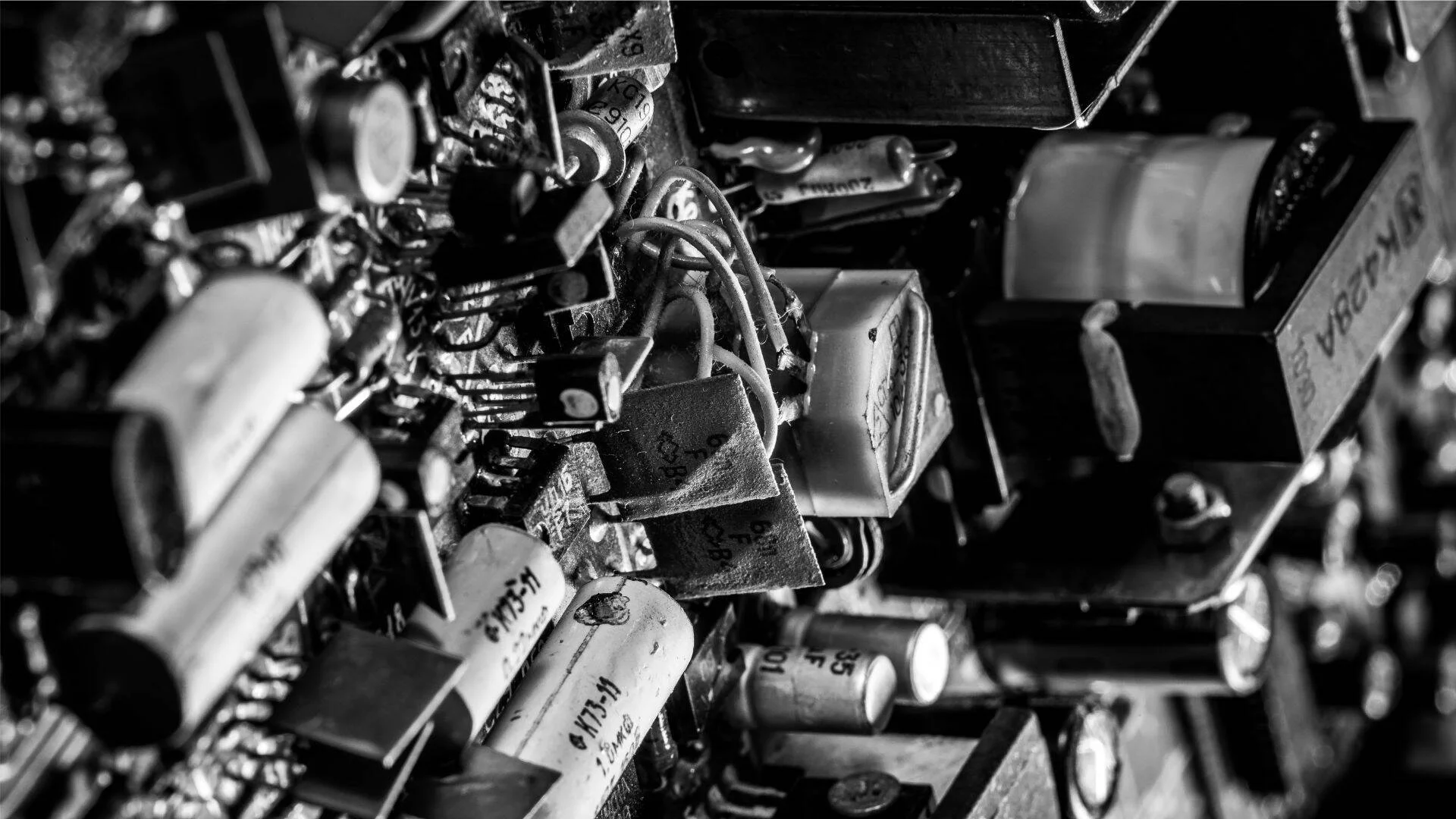 Primer plano en blanco y negro de una placa de circuito con capacitores, transistores y cables de equipos electrónicos vintage.