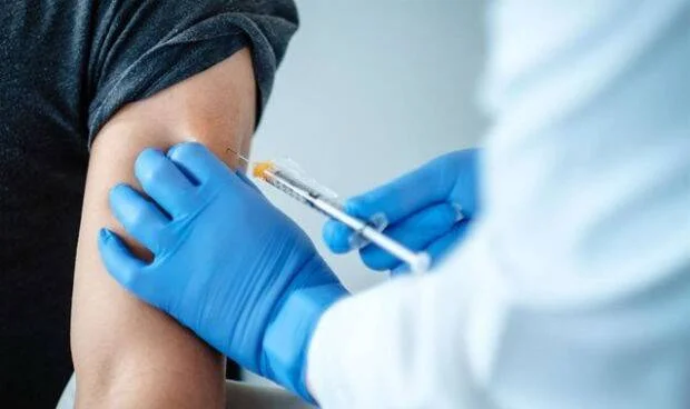 Mano enguantada de un profesional de salud inyectando una vacuna en el brazo de un paciente.