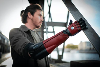 Hombre joven apoya una prótesis de brazo de color rojo y negro sobre una estructura metálica al aire libre.