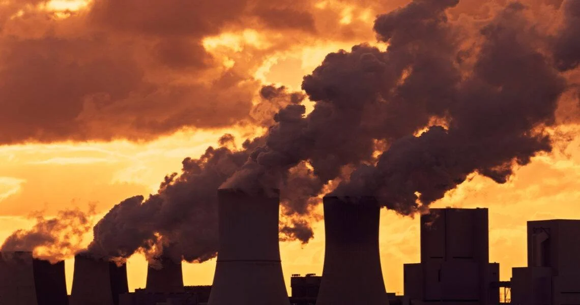 Torres de refrigeración de una central térmica expulsan grandes columnas de humo bajo un cielo naranja al atardecer.