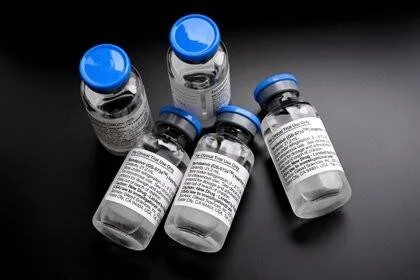 Cinco viales de medicamento con tapas azules y etiquetas técnicas sobre superficie oscura.