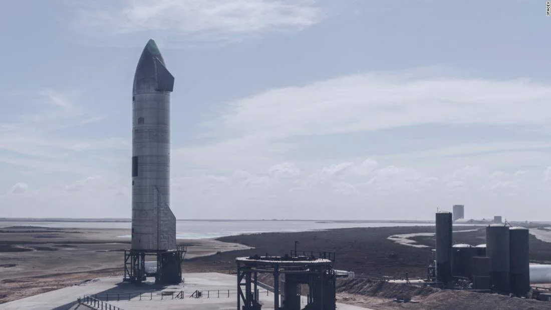 Prototipo de cohete Starship de SpaceX erguido en la plataforma de lanzamiento en Boca Chica, Texas, con paisaje costero de fondo.