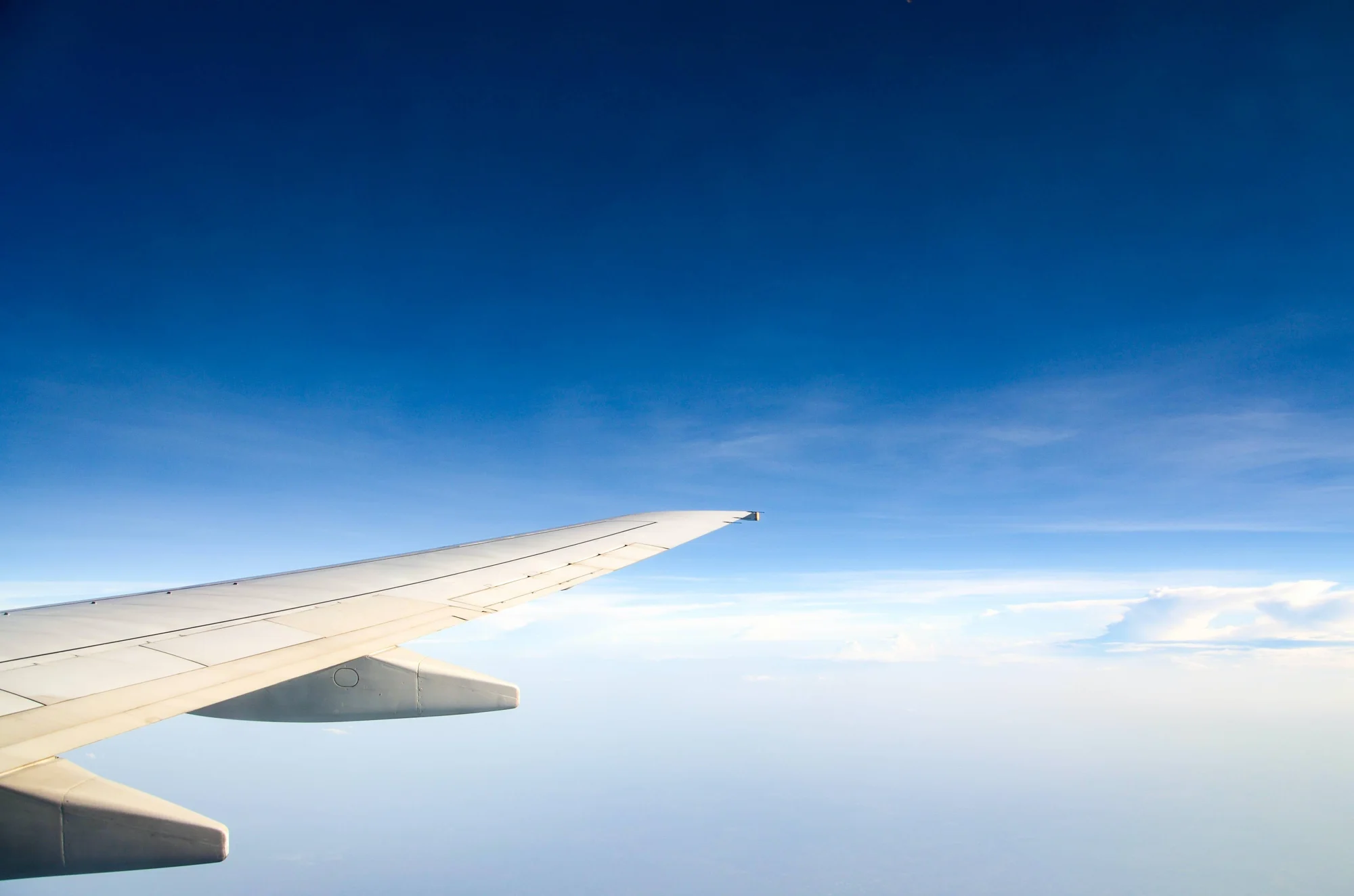 Vista desde la ventanilla de un avión mostrando el ala blanca sobrevolando nubes bajo un cielo azul intenso.