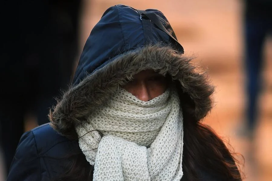 Persona cubriendo su rostro con una gruesa bufanda de lana y campera con capucha forrada en piel, protegiéndose del intenso frío.