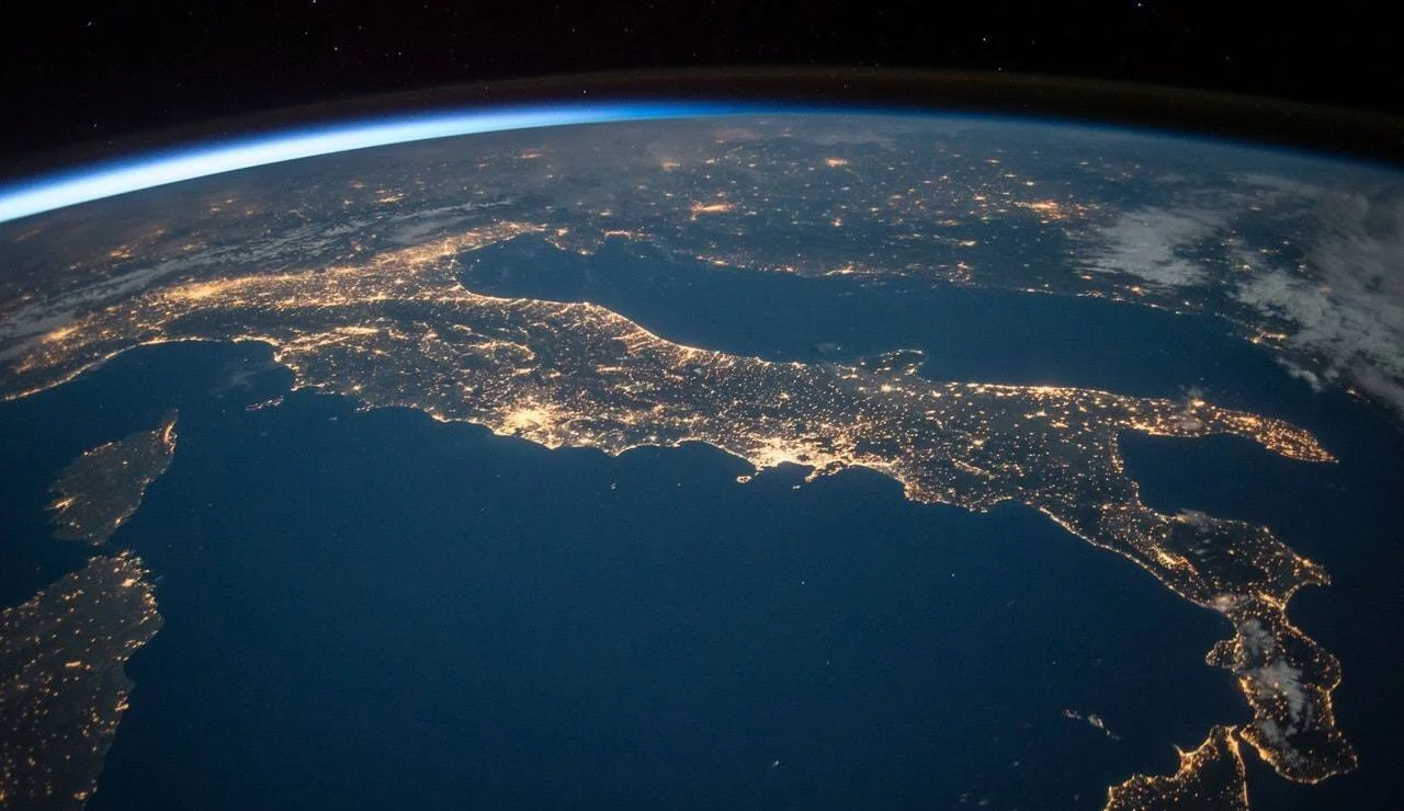 Vista nocturna de la península itálica desde el espacio, con las luces de las ciudades iluminando su contorno sobre el mar Mediterráneo.