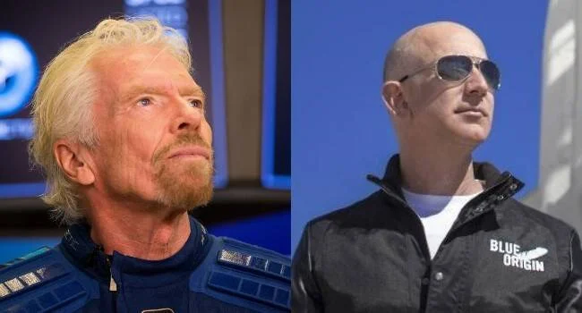 Dos hombres posando: uno con traje espacial azul y otro con chaqueta de Blue Origin y gafas de sol.