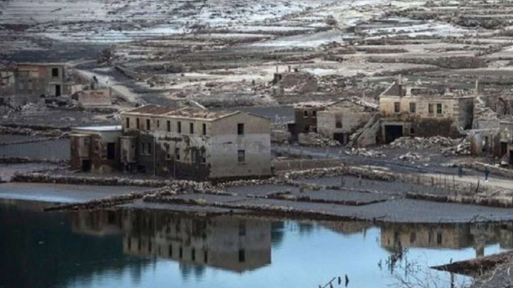 Ruinas de un pueblo sumergido que emergen al bajar el nivel del agua de un embalse, con edificios deteriorados reflejados en el agua.