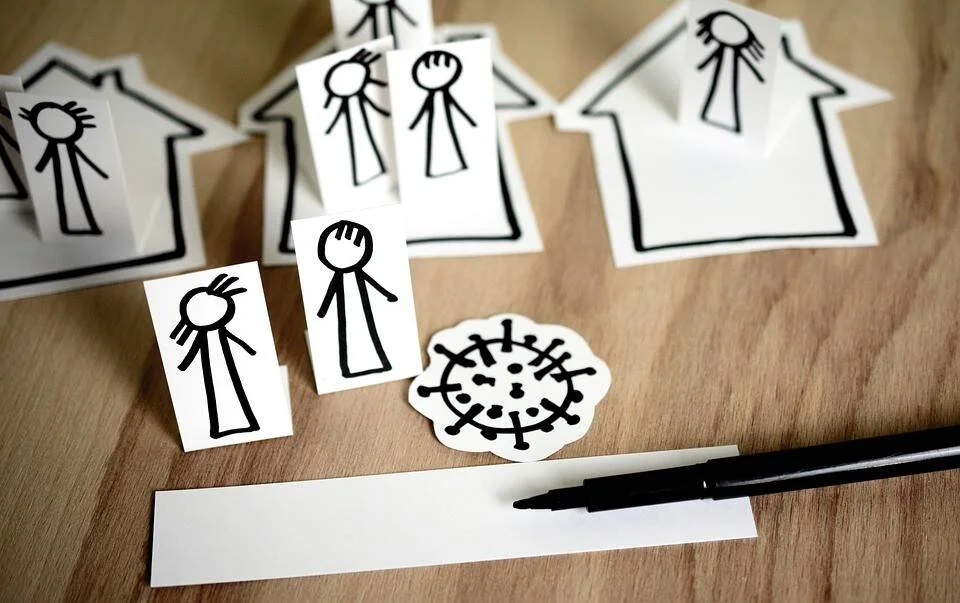 Recortes de papel con figuras palito, casas y un dibujo de virus, representando el aislamiento social durante una pandemia.
